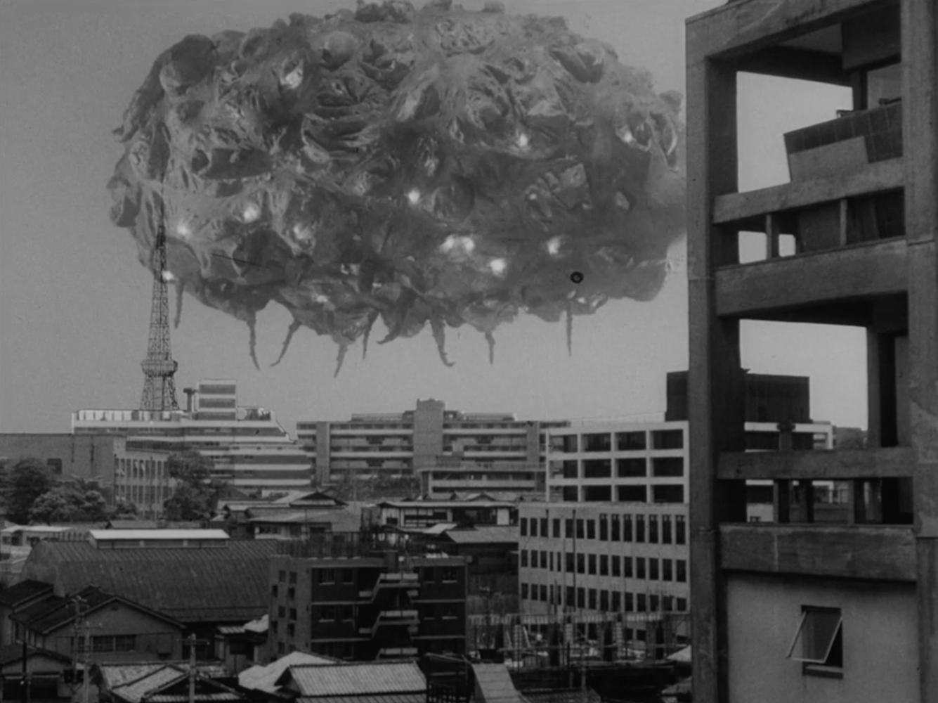 The giant form of Balloonga floats over Tokyo. Tokyo tower is visible, showing the creature's immense size.